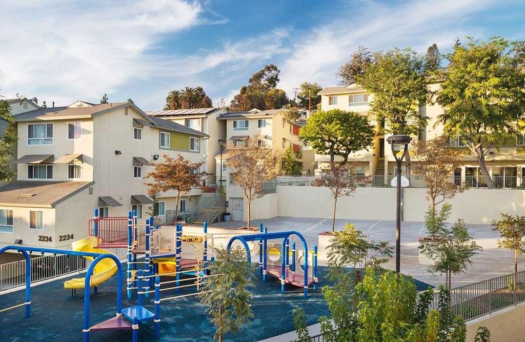 A playground with a blue slide and a yellow slide in front of apartment buildings.