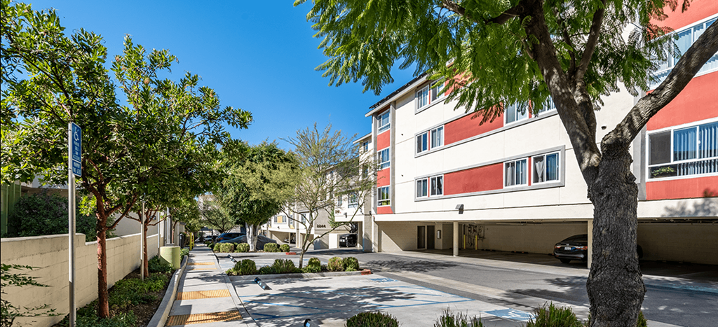 a street view of an apartment building with trees and a sidewalk at Mission Plaza Apartments
