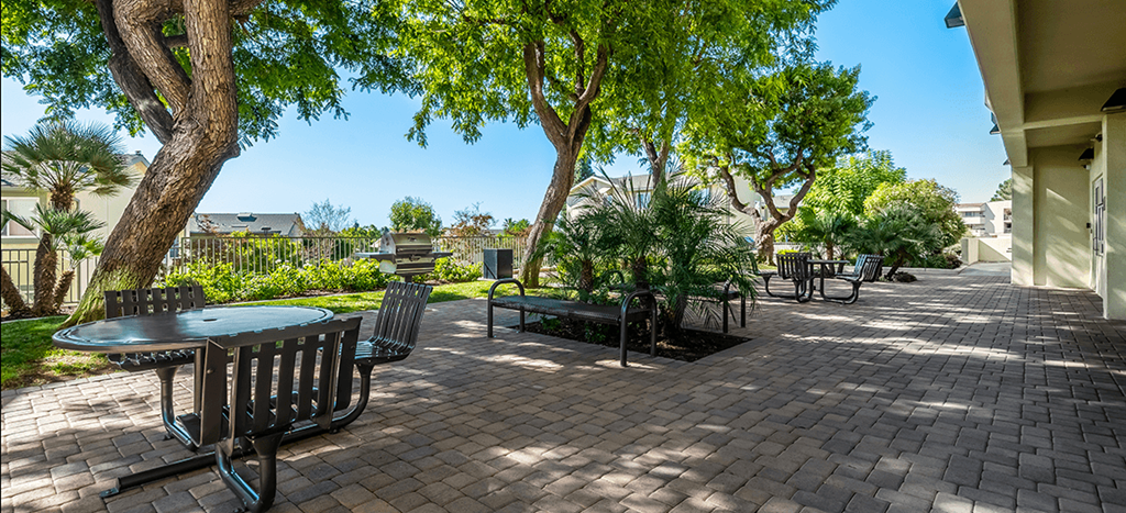 a patio with tables and chairs and trees at Mission Plaza Apartments