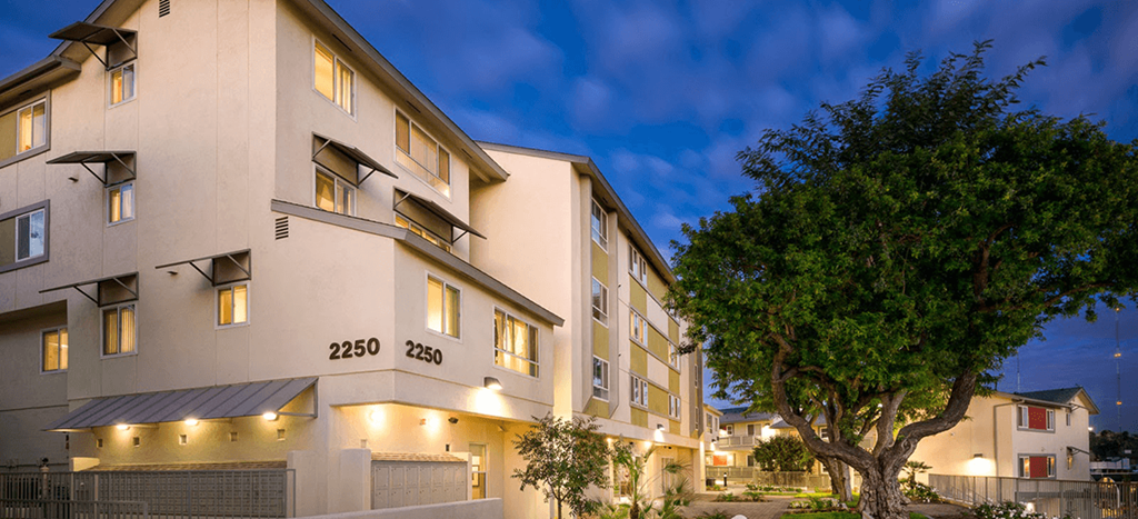 Mission Plaza Apartment buildings along a tree-lined street at dusk