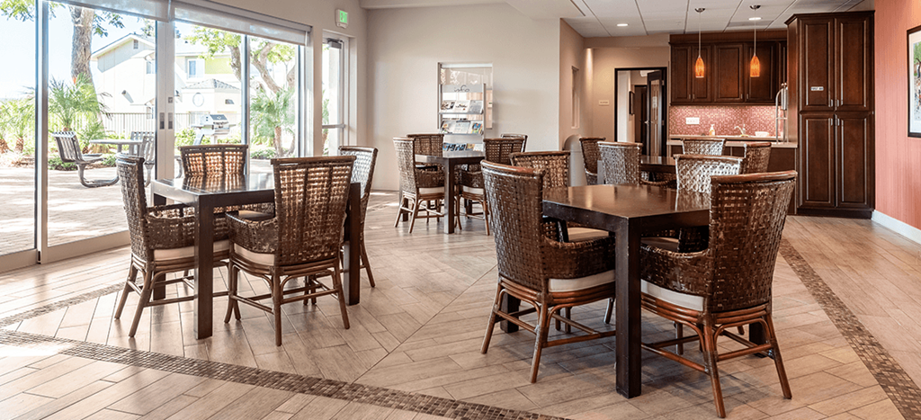 Mission Plaza Apartments clubhouse with tables and chairs and a large window and a kitchenette in the background