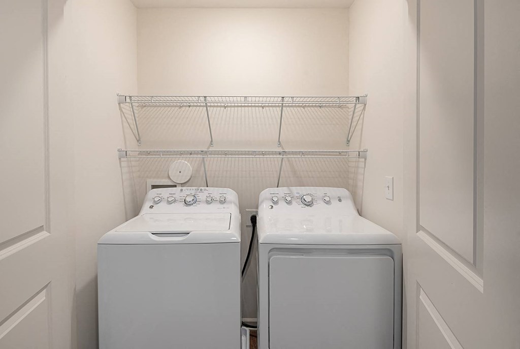 two washers and a dryer in a laundry room with a shelf above