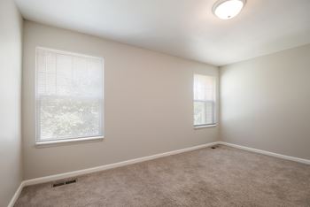 A room with a carpeted floor and two windows.
