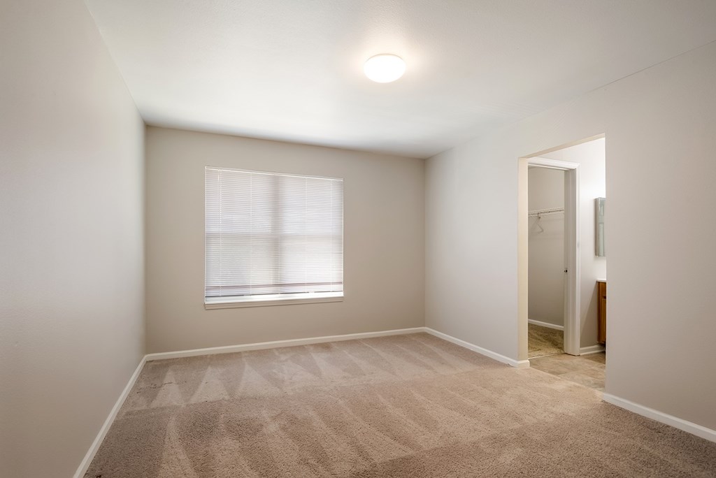 A room with a carpeted floor and a window with blinds.