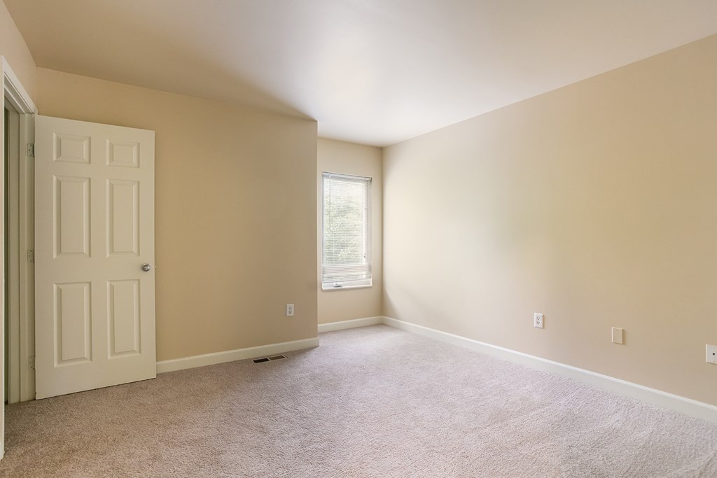 A room with a white door and a window with a view of trees outside.
