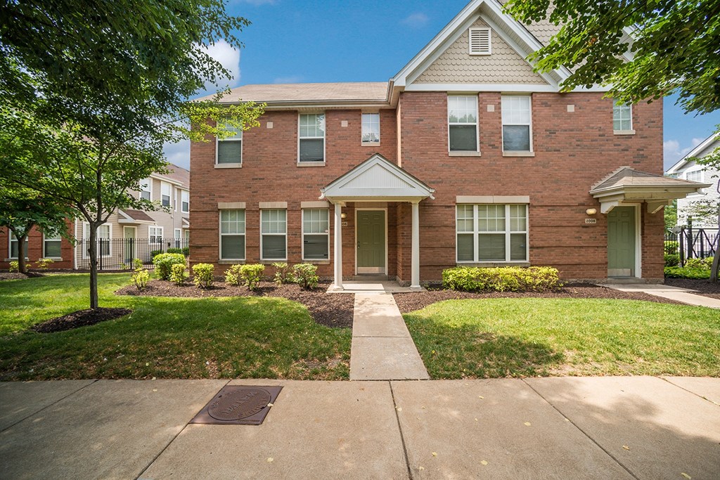 front view of a brick apartment building with a sidewalk and grass