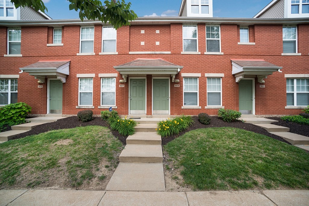 the front of a brick apartment building with stairs and grass