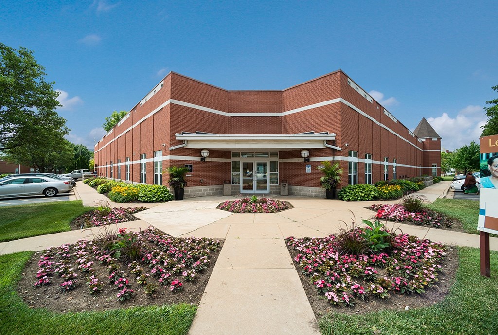 the front of a brick building with a sidewalk and flower gardens