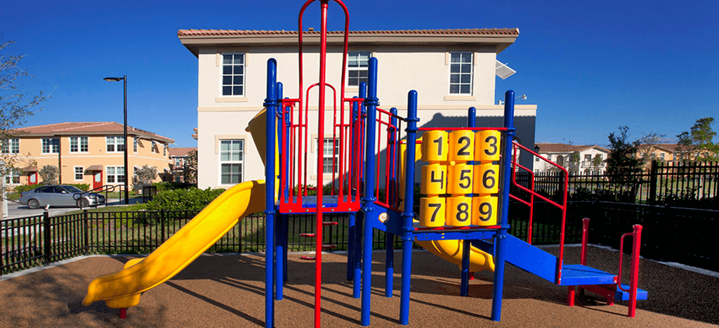 a playground in front of an apartment building with a yellow slide at Northpark at Scott Carver Apartments