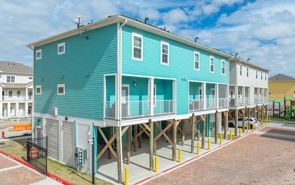 a blue house sitting on stilts in front of a parking lot