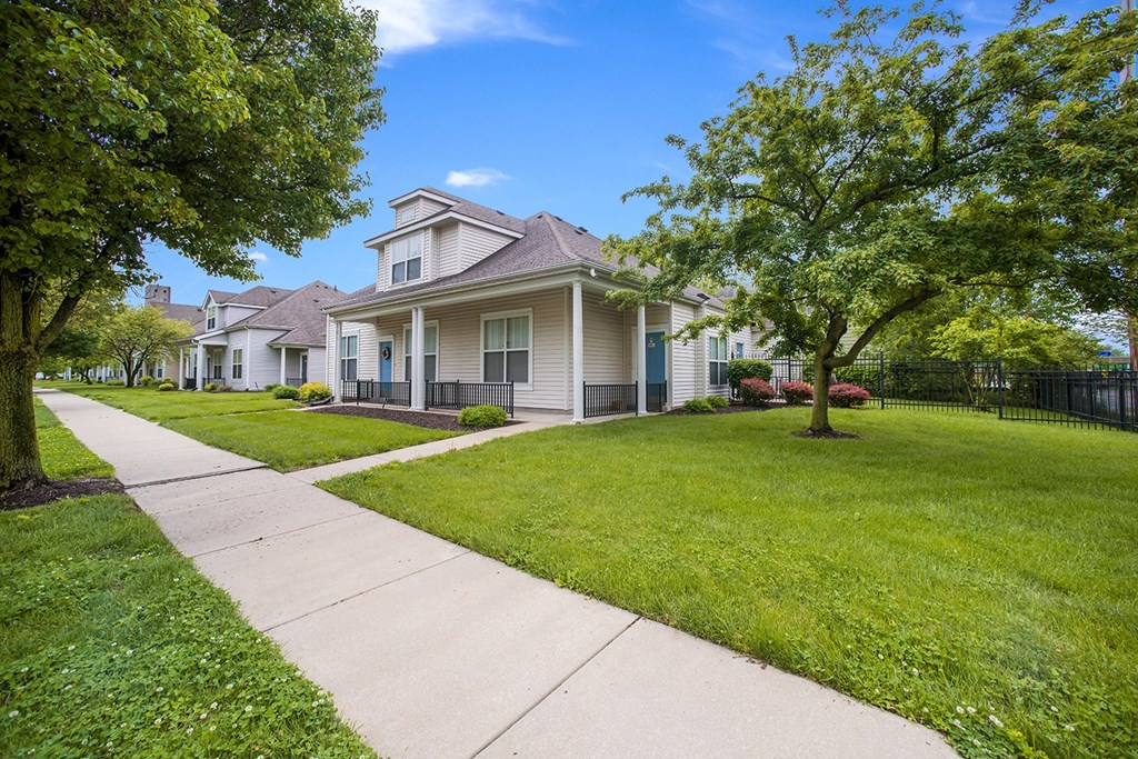 a white house with a sidewalk and grass lawn and trees
