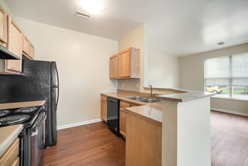 an empty kitchen with wood flooring and a black refrigerator