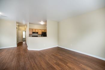 an empty living room with wood flooring and a kitchen