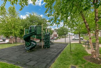 A playground with a green slide and a black mat.