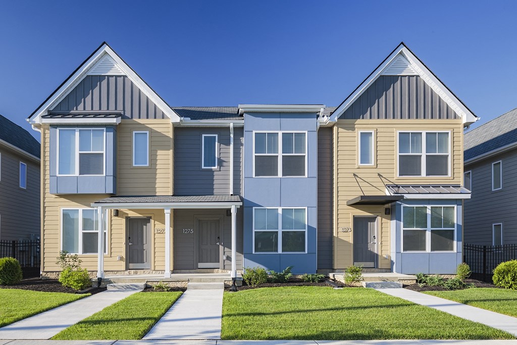 a row of houses with a green lawn and a blue sky at Legacy Pointe at Poindexter Apartments & Townhomes