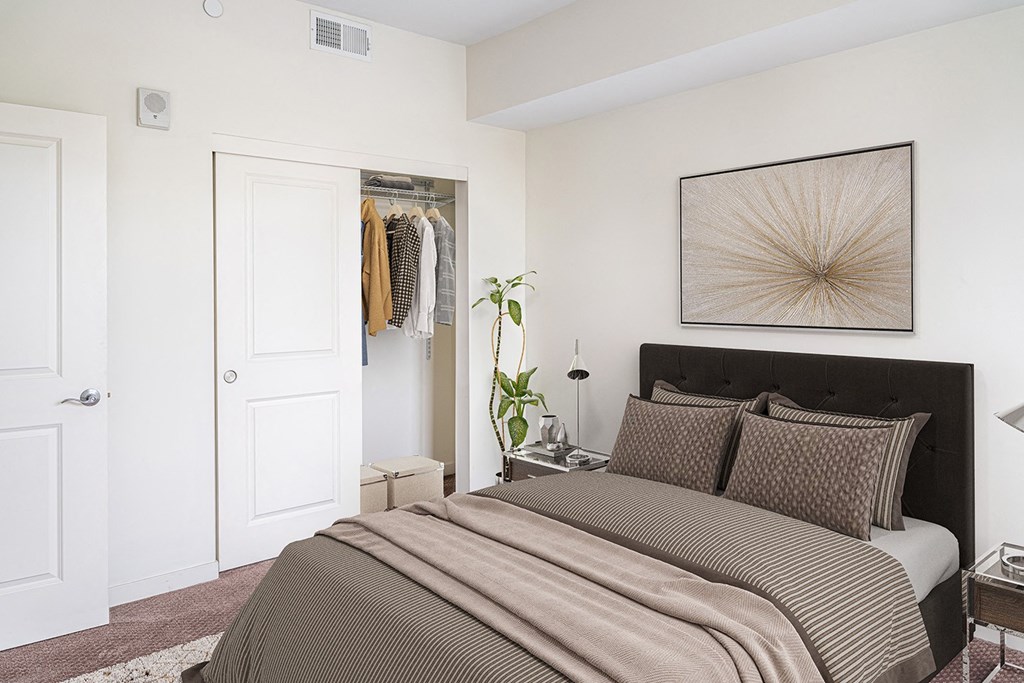 a bedroom with a queen bed and art on the wall and an open closet at Legacy Pointe at Poindexter Apartments & Townhomes