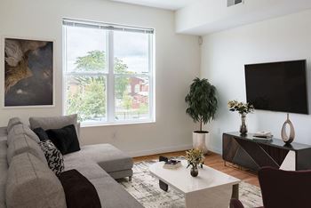 A living room with a grey couch, a white coffee table, and a large window.