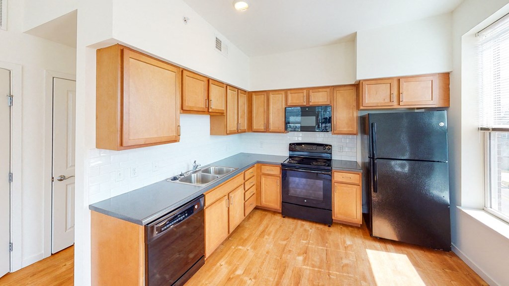 a kitchen with wood cabinets and a stone counter top with black appliances and wood flooring at Legacy Pointe at Poindexter Apartments & Townhomes