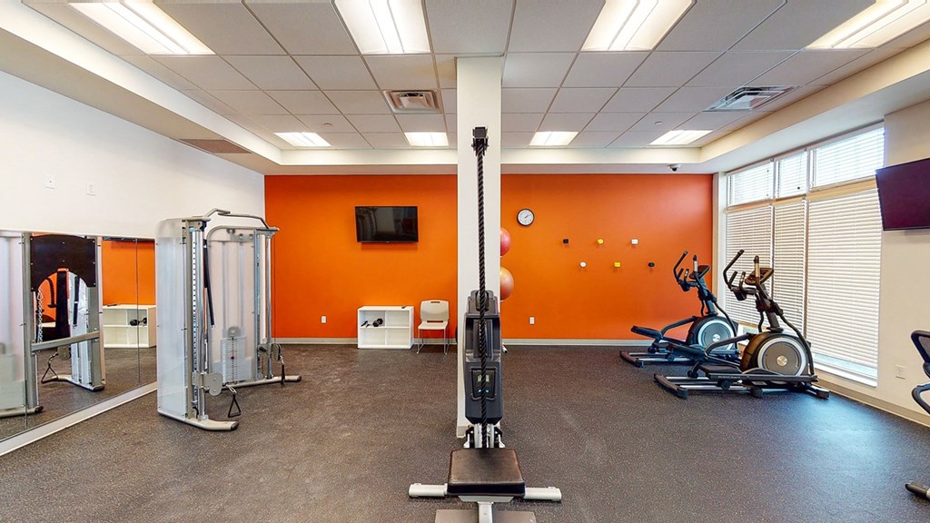 a gym with weights and cardio equipment in a building with orange walls at Legacy Pointe at Poindexter Apartments & Townhomes