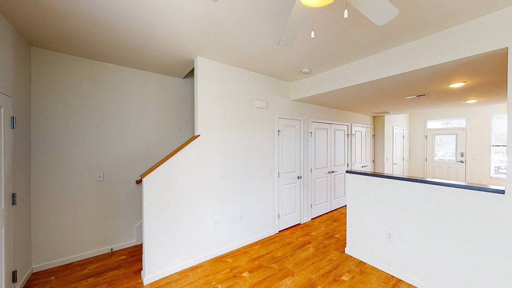 a living room with a white wall and a ceiling fan at Legacy Pointe at Poindexter Apartments & Townhomes