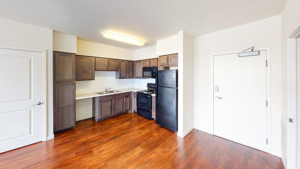 an empty kitchen with wood flooring and a black refrigerator at Legacy Pointe at Poindexter Apartments & Townhomes