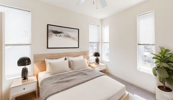 A bedroom with a large bed, a nightstand with a lamp, and a plant.