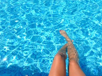 A person's legs are submerged in clear blue water.