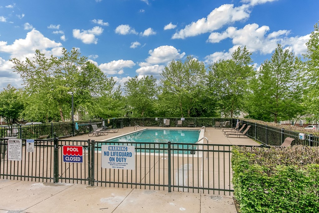 A pool surrounded by a black fence with a sign that says pool closed and no lifeguard on duty.