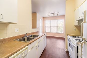 an empty kitchen with white appliances and wooden floors