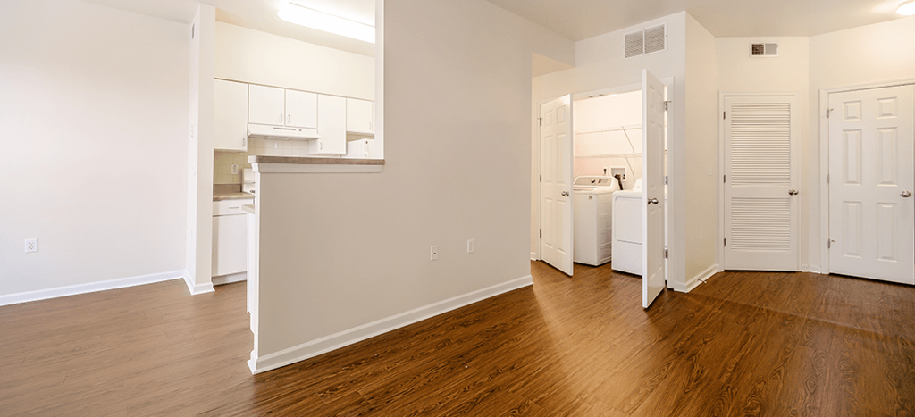 an empty living room and kitchen with wood floors and white cabinets at Renaissance Place at Grand Apartments
