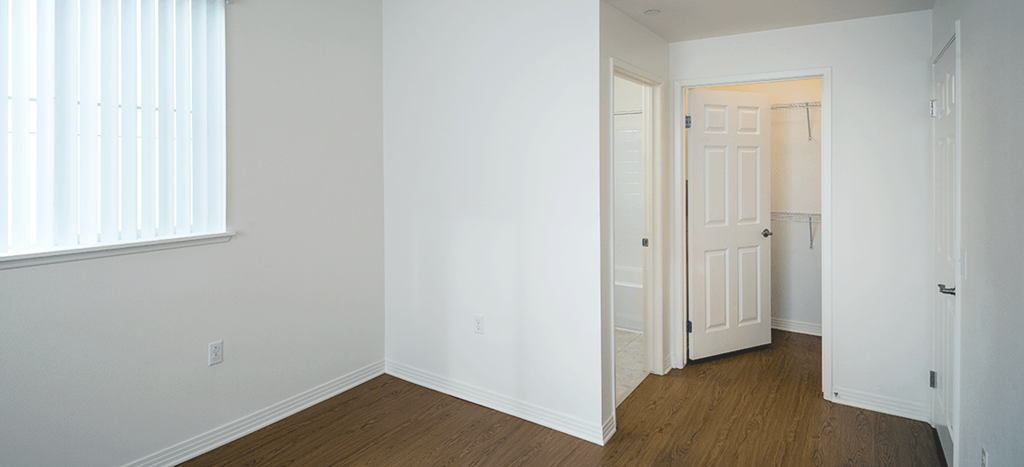an empty bedroom with white walls and wood flooring and a white door to a closet with shelving