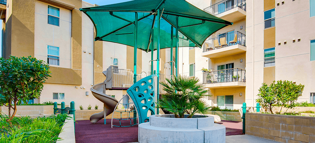 a playground at Santa Cecilia Apartments with a large green umbrella