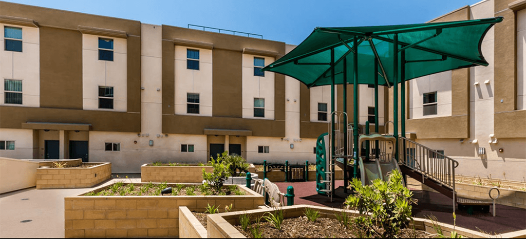 a large building with a playground and a green umbrella in the courtyard of Santa Cecilia Apartments