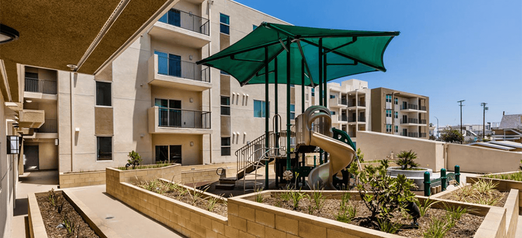 Playground at Santa Cecilia Apartments with a green awning and beige slide in a courtyard