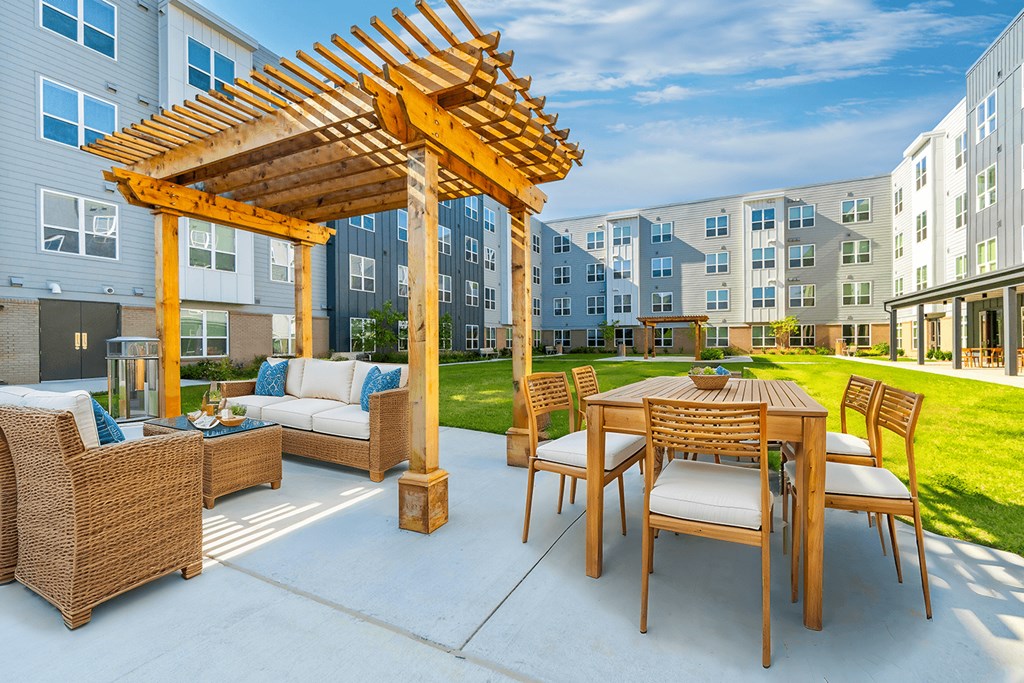 A wooden pergola is over a patio table with chairs.