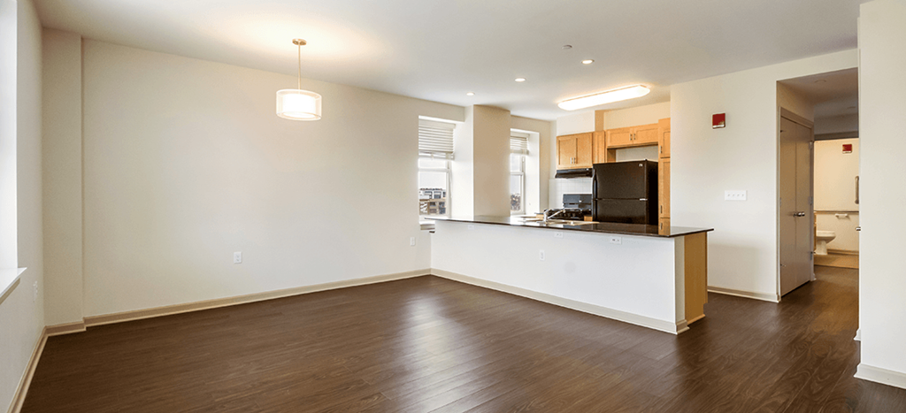 the living room and kitchen of an empty apartment with wood flooring and white walls at The Strathmore Apartments