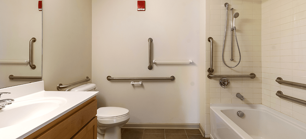 a bathroom with grab bars on the wall and a toilet and a tub and sink at The Strathmore Apartments