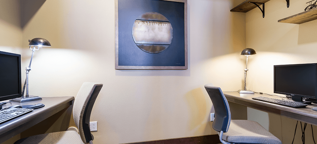 two desks with computers in a office with a painting on the wall