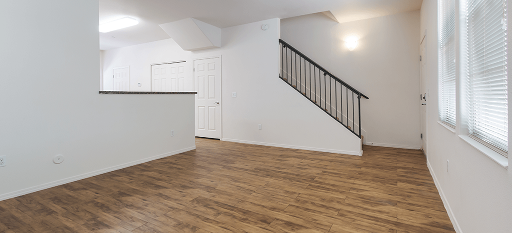 an empty living room with white walls and wood flooring and a staircase at The Symphony Apartments