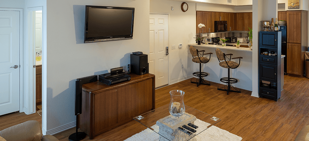 a living room with a television and a kitchen with wooden cabinets and a bar with stools