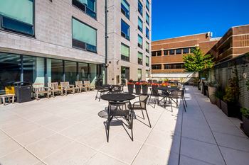 A patio with tables and chairs is surrounded by buildings.
