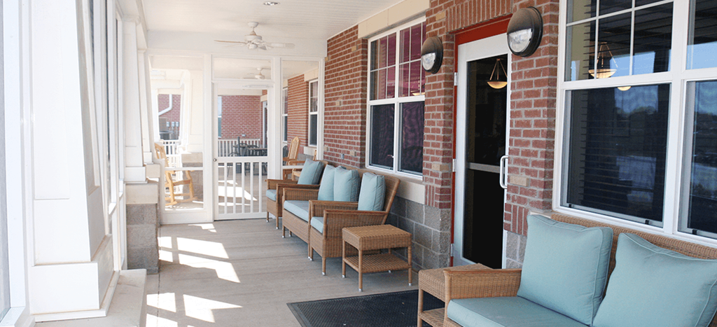 a porch with benches and chairs and a brick building at Senior Living at University Place