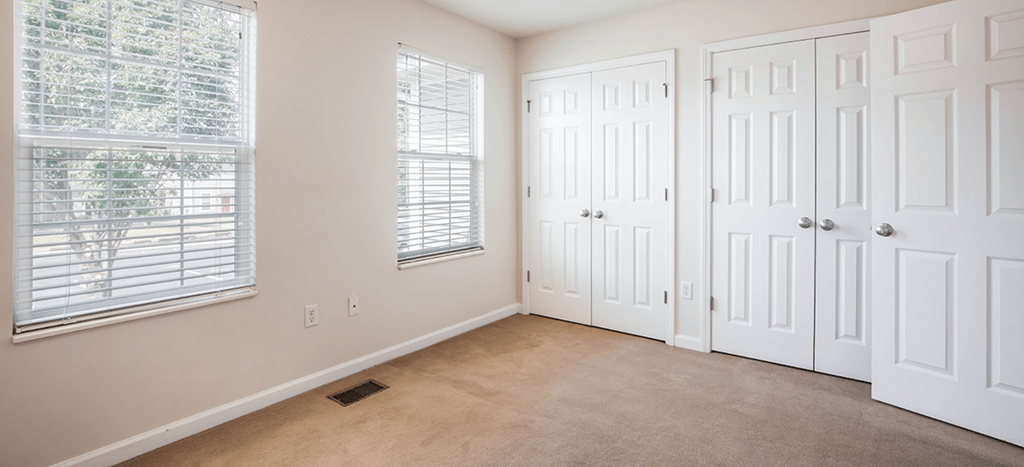 an empty bedroom with two closets and two windows