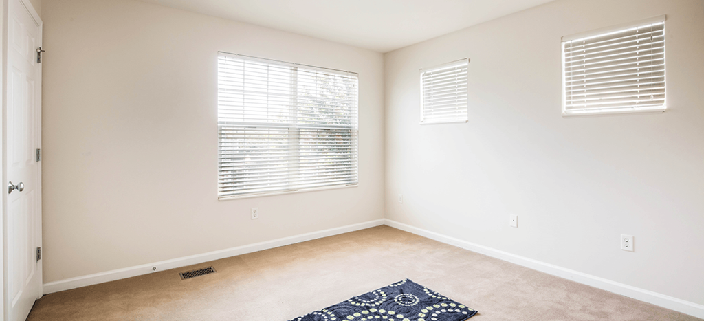 an empty room with two windows and a rug on the floor