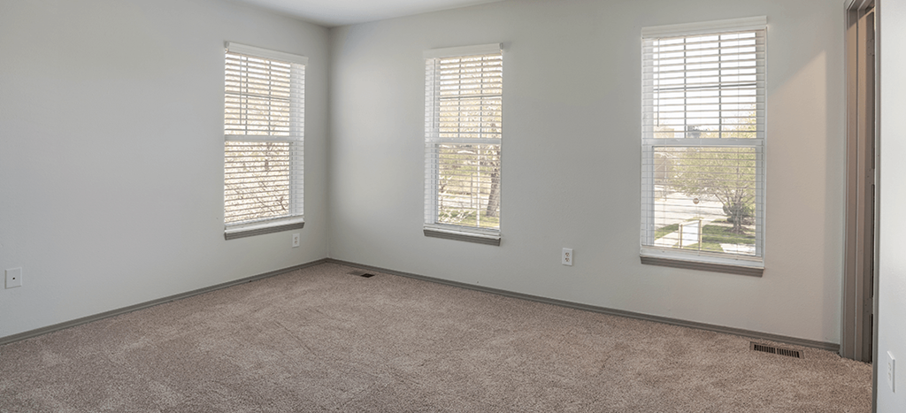 an empty bedroom with three windows and carpet at Villa del Sol Apartments