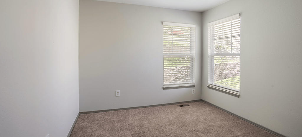 an empty room with two windows and a carpet