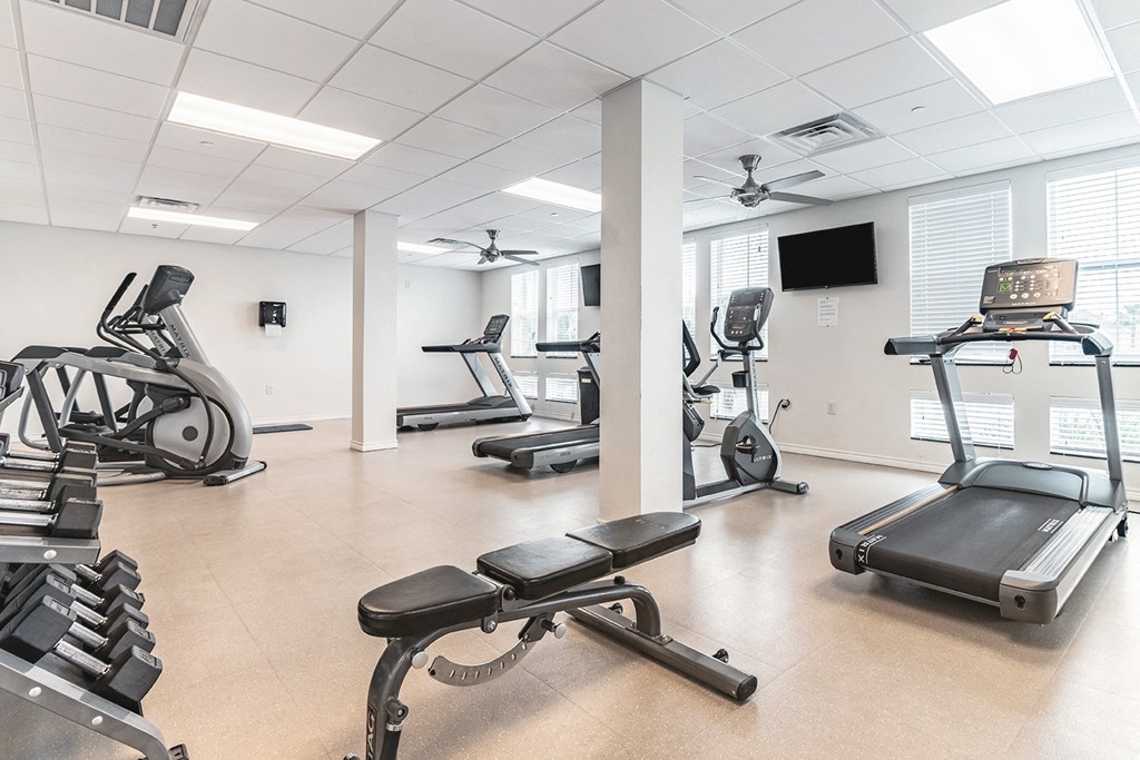 a gym with treadmills and other exercise equipment in a room with windows