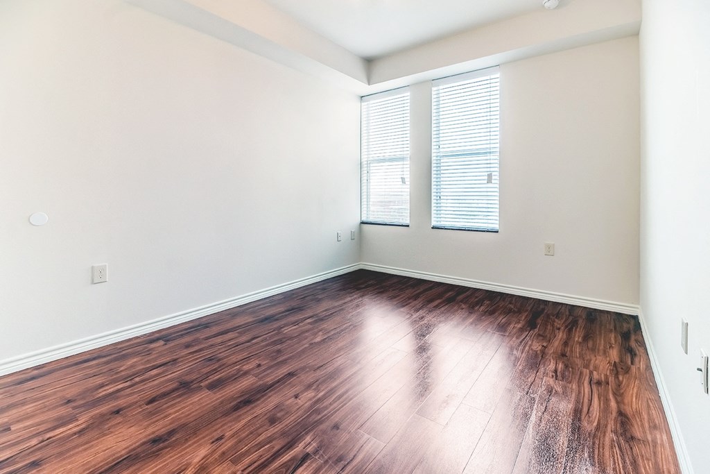 an empty living room with hardwood flooring and two windows