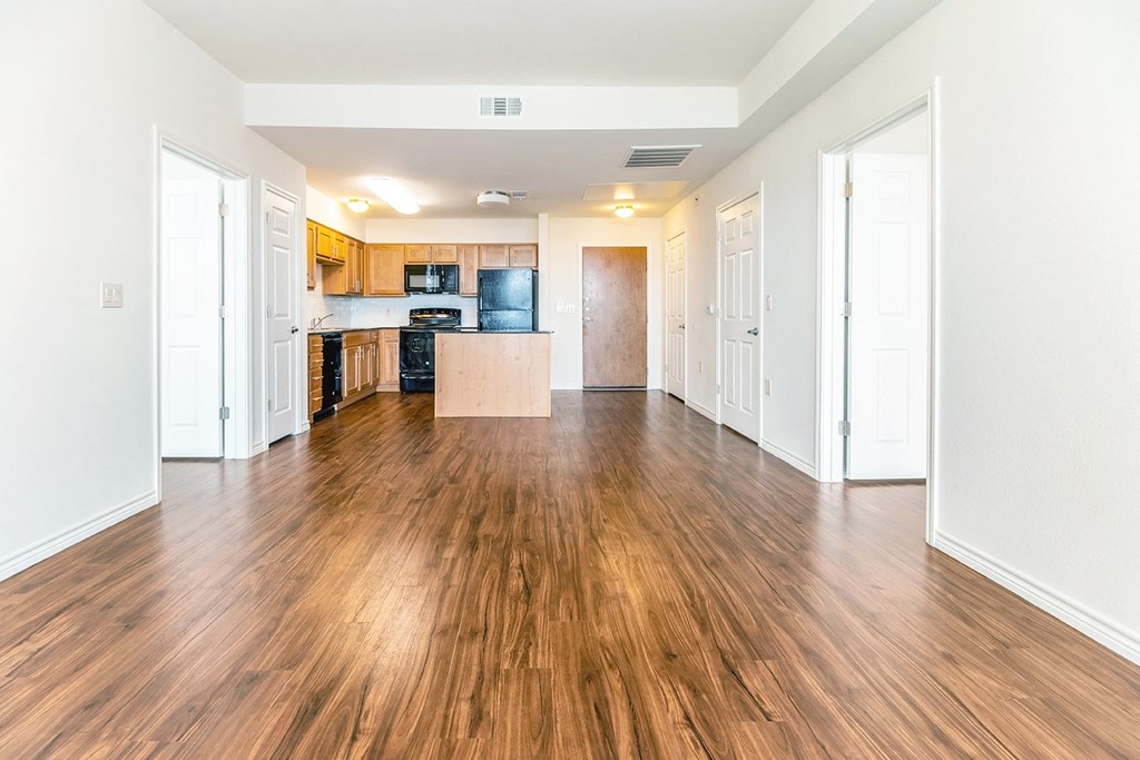 an empty living room and kitchen with wood floors and white walls