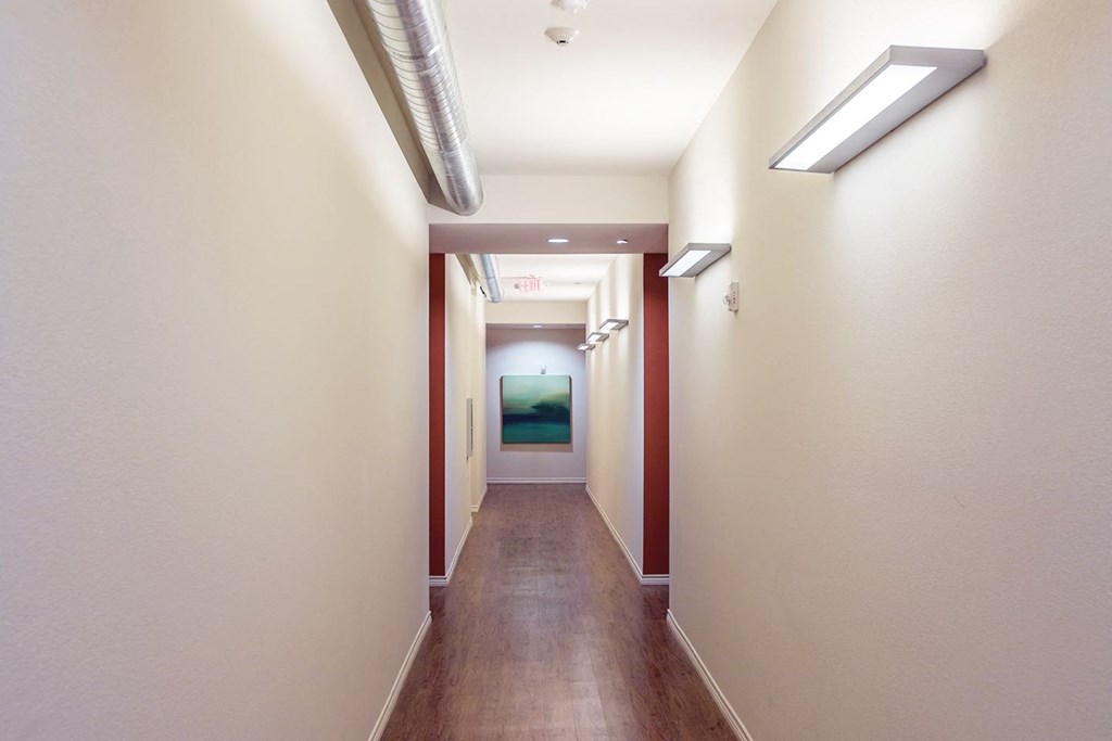 a long hallway with wood floors and white walls and a green room at the end